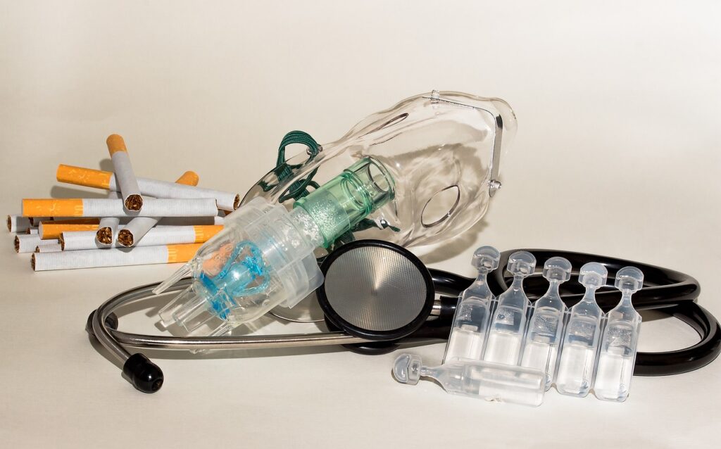 Ein Bild mit Dingen, die typischerweise mit COPD in Verbindung gebracht werden (Stetoskop, Beatmungsmaske, Zigaretten, Medikamente)