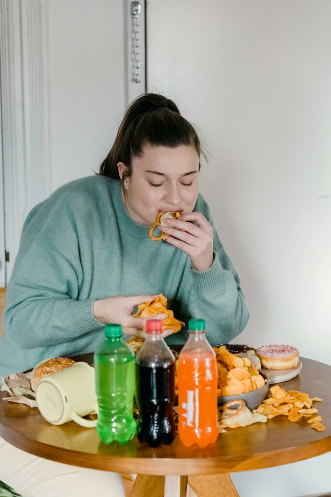 Ein Frau, die von ungesundem Essen und Trinken umgeben ist und davon isst.